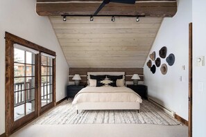 Een slaapkamer met een groot raam, een bed met een geborduurde plaid en een wand met verschillende hoeden.
