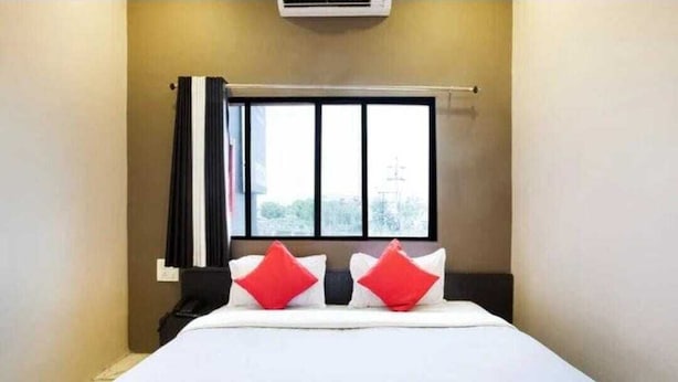 Una camera d'albergo con un letto, una finestra con tende e un condizionatore d'aria a parete.