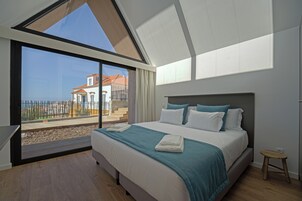 Un dormitorio moderno con una cama grande, vista a un edificio por una puerta de cristal y piso de madera.