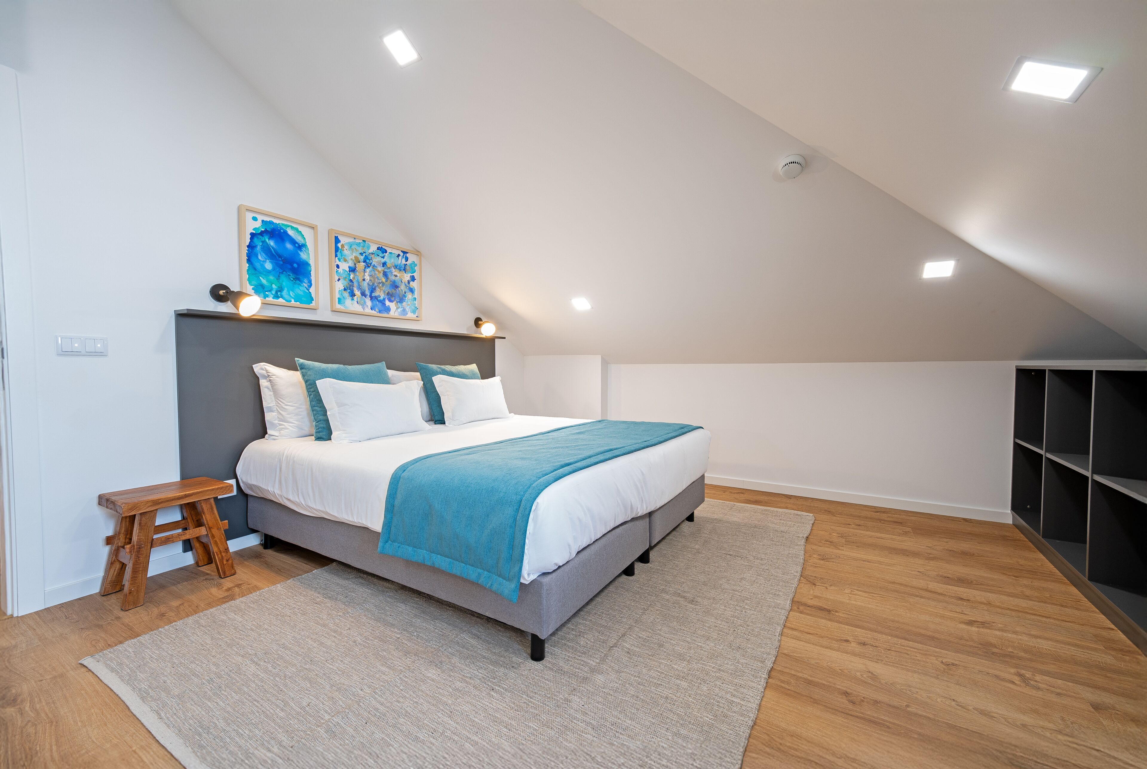 Ein Schlafzimmer mit einem Bett, einem Nachttisch, einem Holzschemel und einem grauen Teppich.