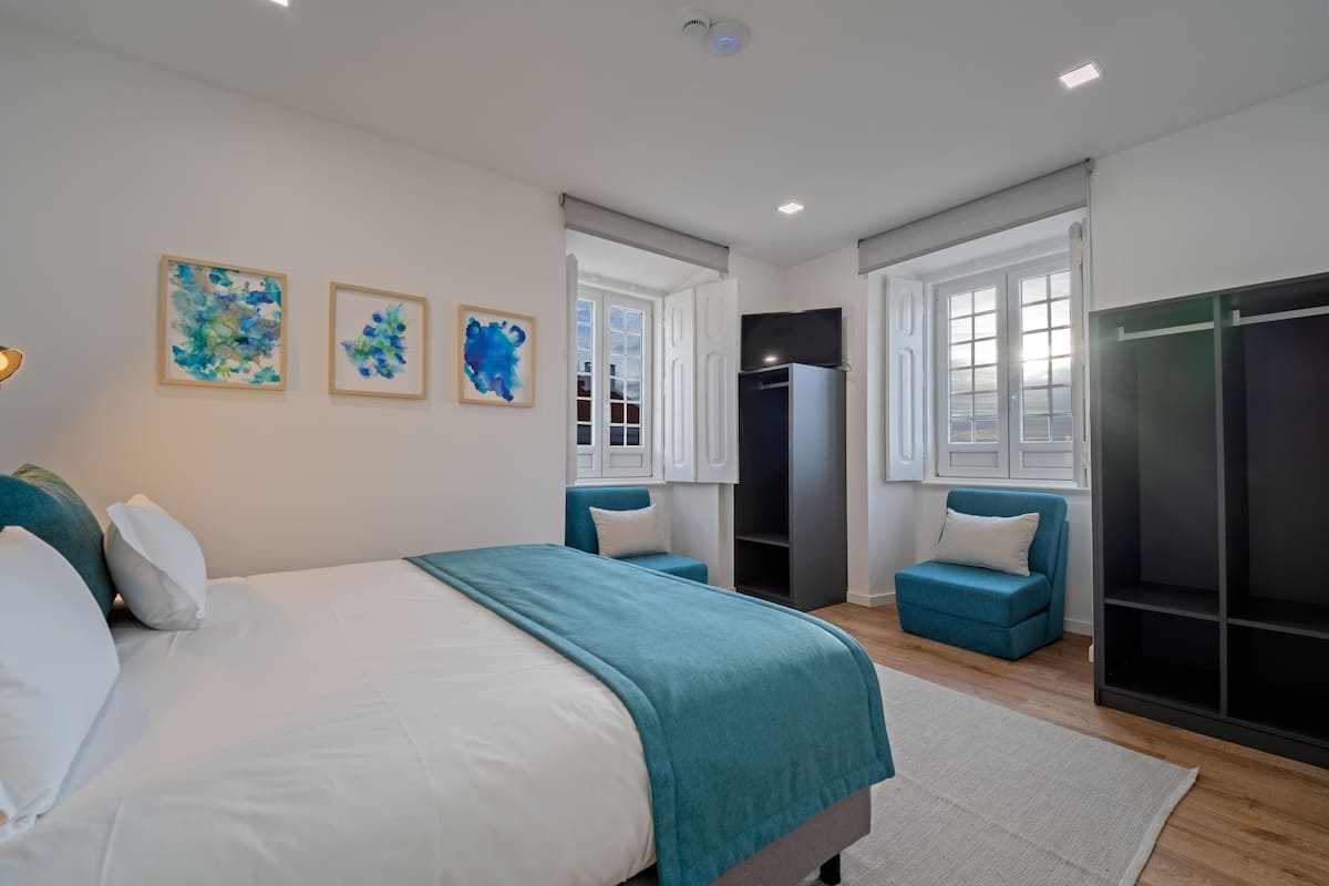 Ein modernes Schlafzimmer mit einem großen Bett, einem Kleiderschrank, einer Sitzecke und Bildern an der Wand.