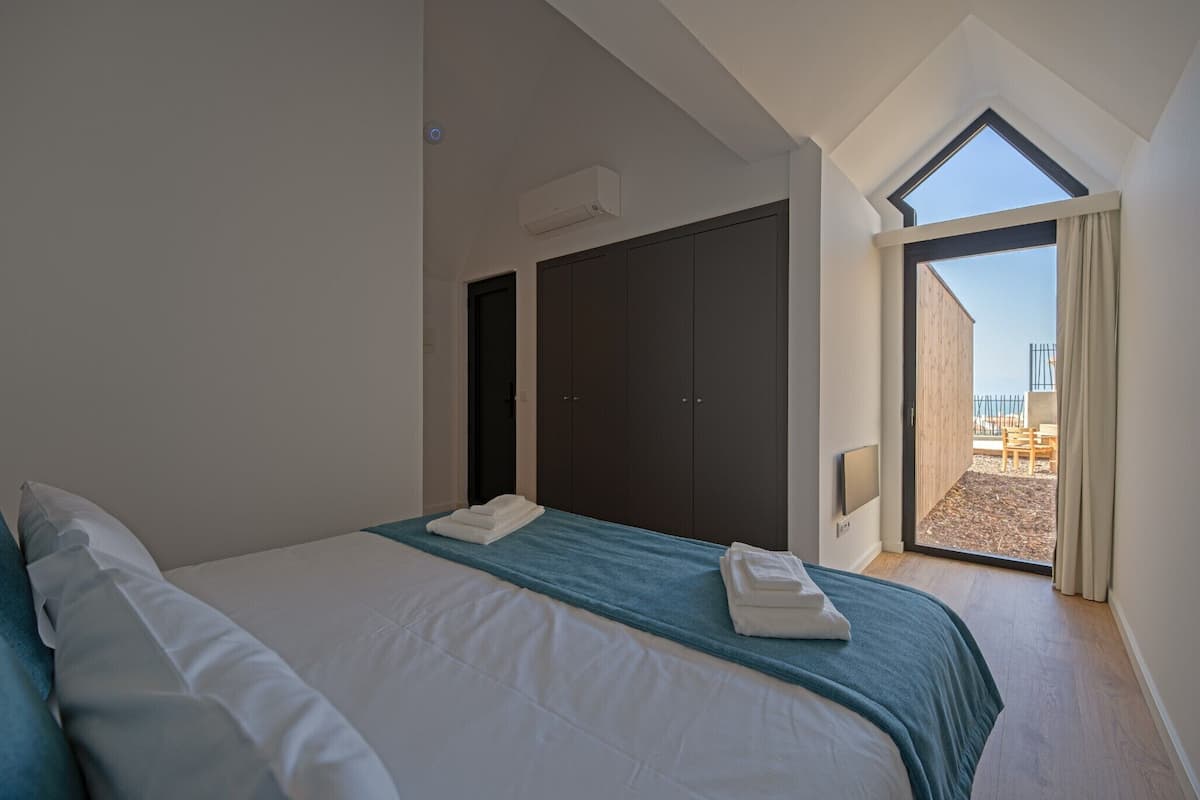 Ein Schlafzimmer mit Bett, Kleiderschrank, Oberlicht und Blick ins Freie.