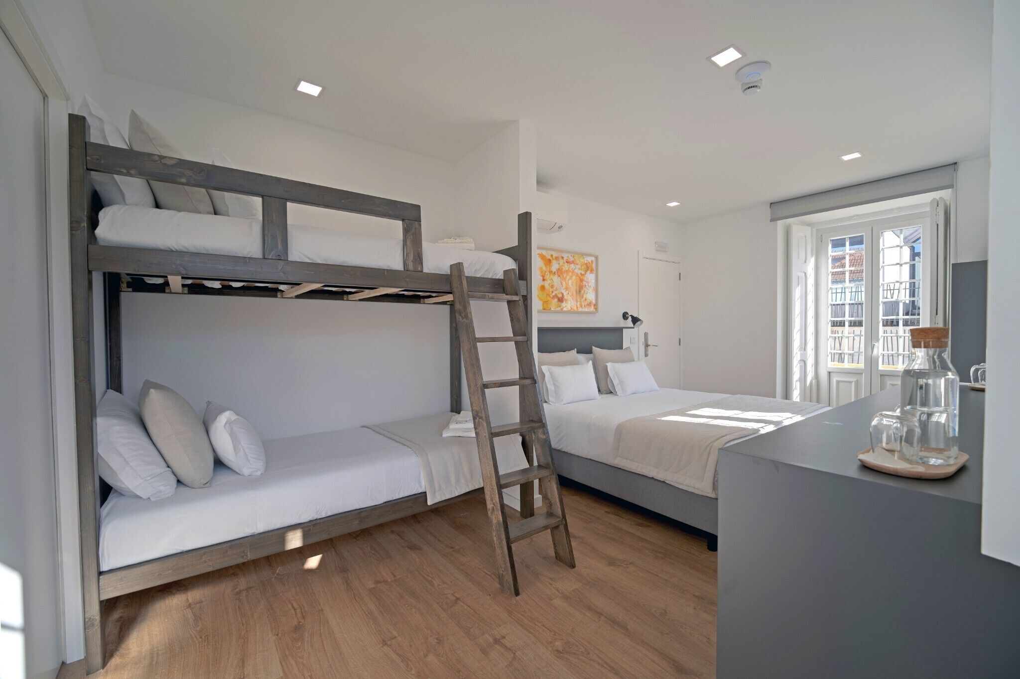 A bunk bed room with a ladder, a desk with a lamp, and a window with a view.