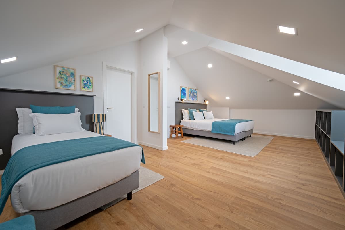 Ein Schlafzimmer mit schrägem Dach, zwei Betten, Holzboden und Bildern an den Wänden.