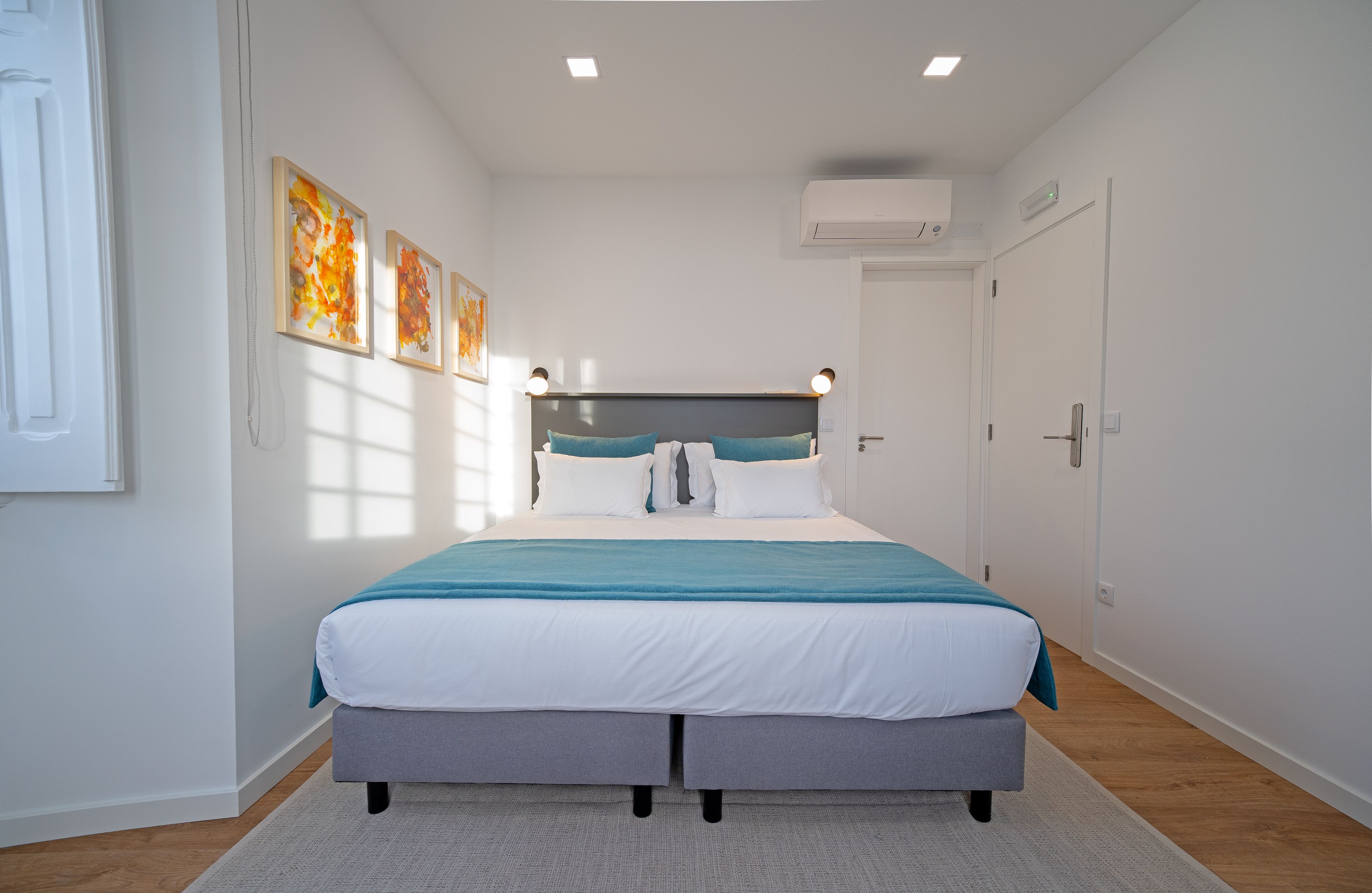 Un dormitorio moderno con una cama grande, un cabecero con luces, una ventana con persianas y una puerta con equipo de aire acondicionado.