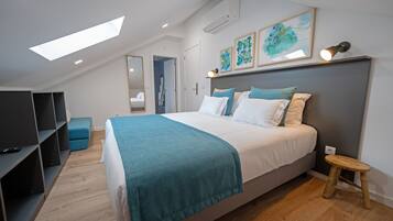 Un dormitorio moderno con tragaluces, una cama con una manta verde azulada, un taburete pequeño y un televisor sobre una estantería.