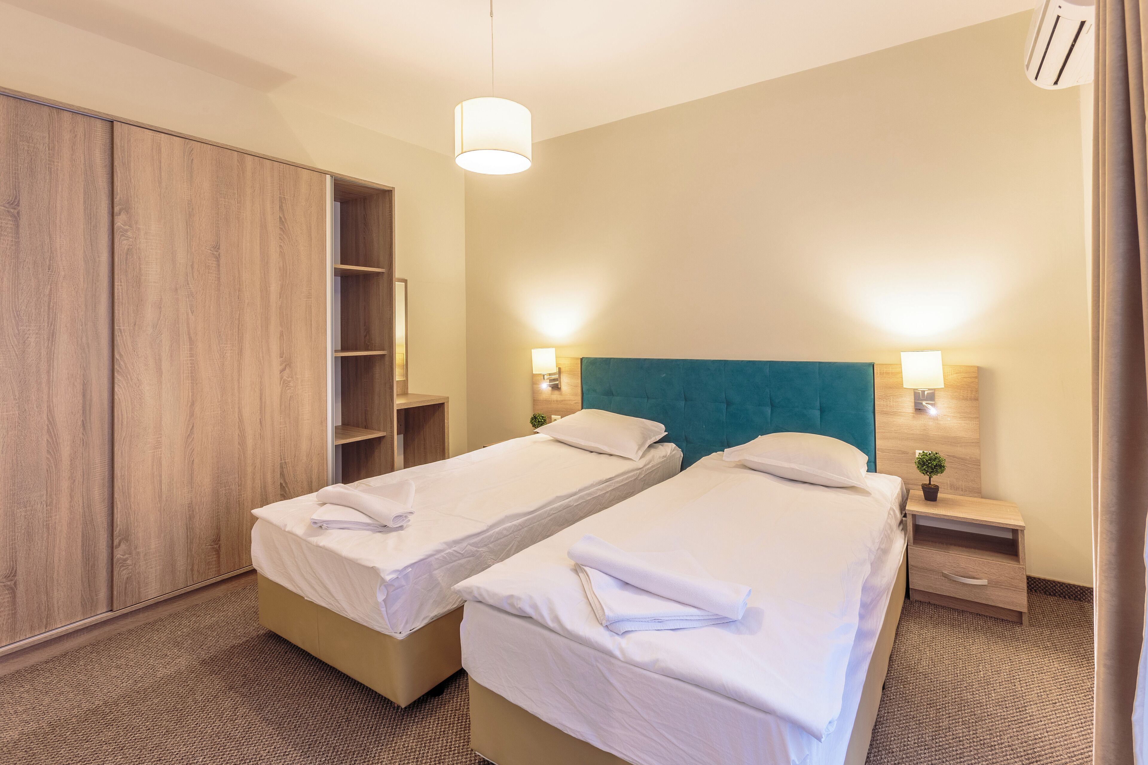 A hotel room with two single beds, a wardrobe, a nightstand with a lamp, and a ceiling light.