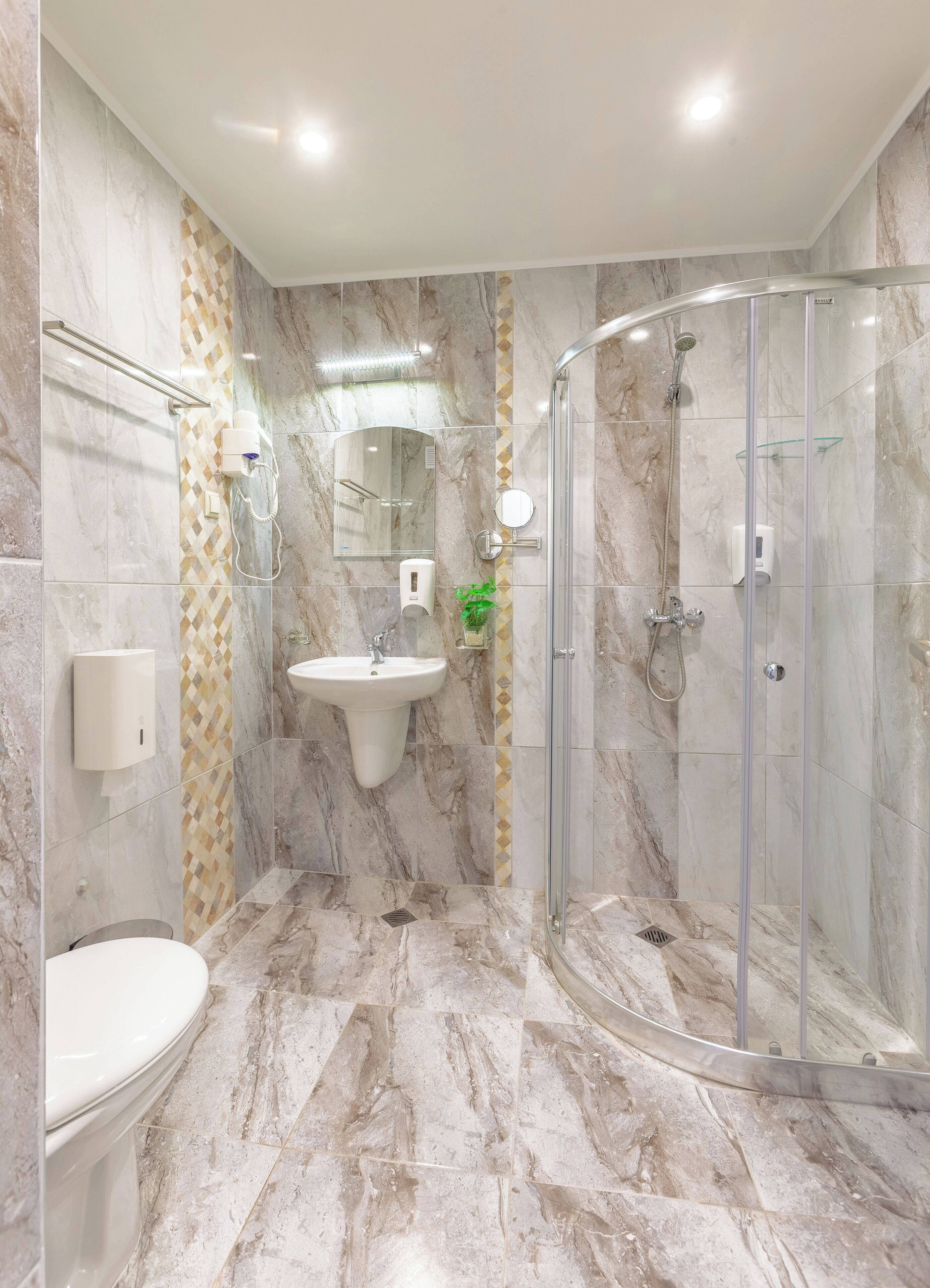 Un baño moderno con cabina de ducha de vidrio, lavamanos pedestal y retrete.