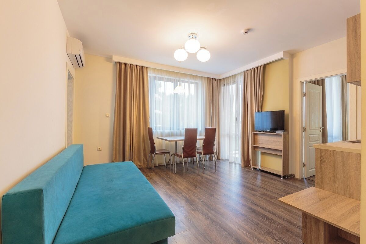 A modern hotel room with a sofa, a dining table with chairs, a TV, and a wooden cabinet.