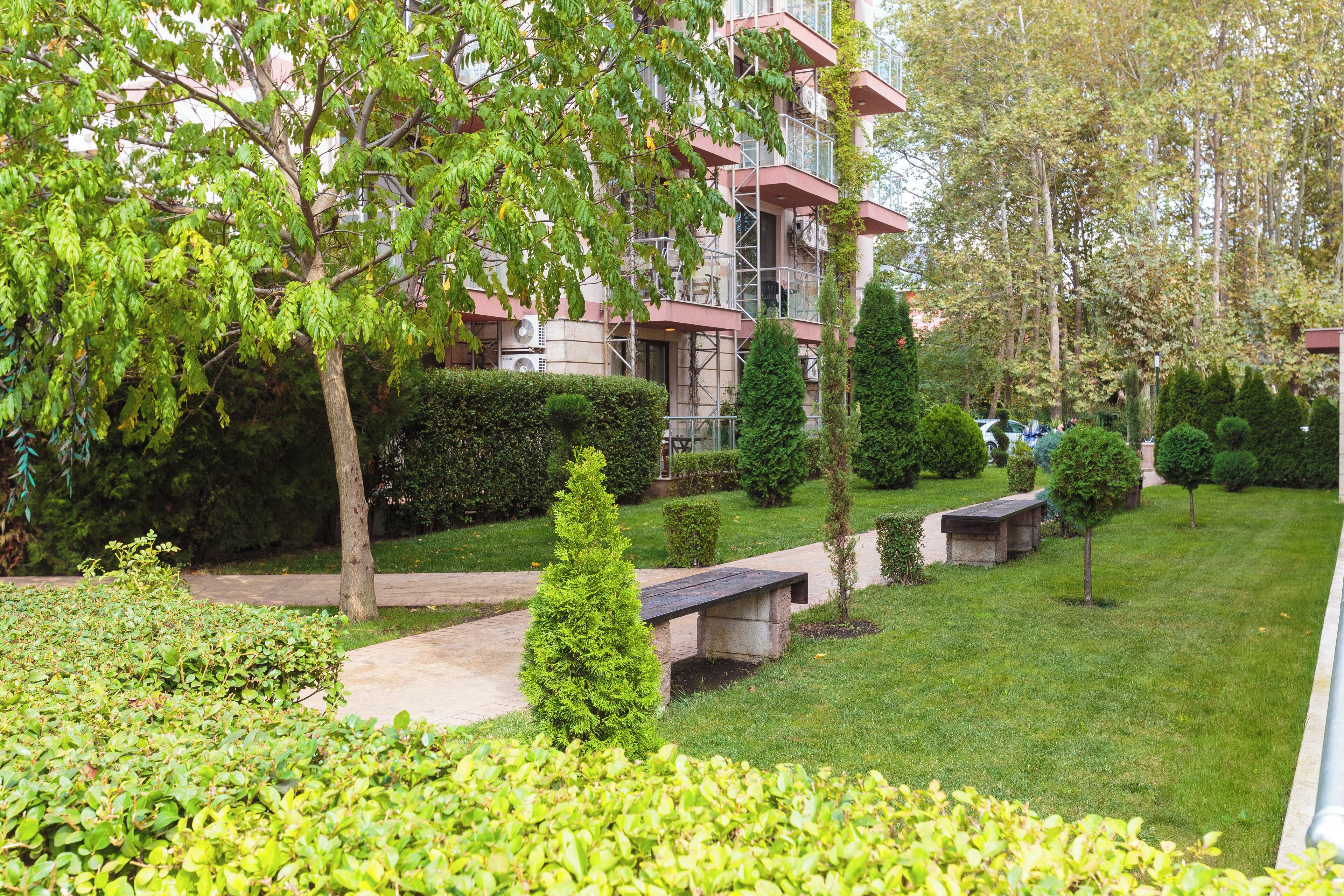 Un jardin bien entretenu, agrémenté d’un sentier, de bancs et d’un bâtiment doté de plusieurs balcons.