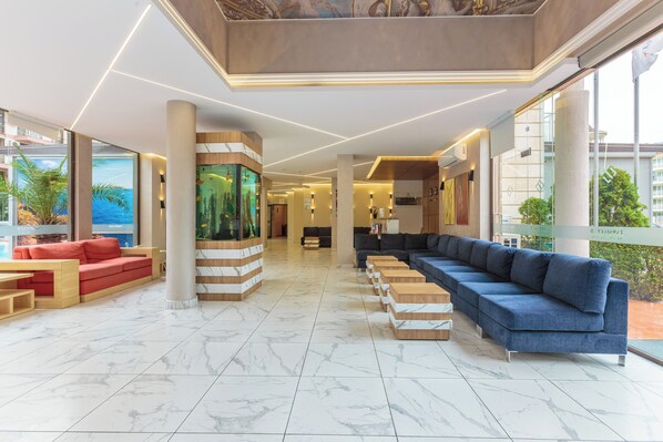 A spacious lobby with a long blue sofa, a red sofa, and a wooden bench area.