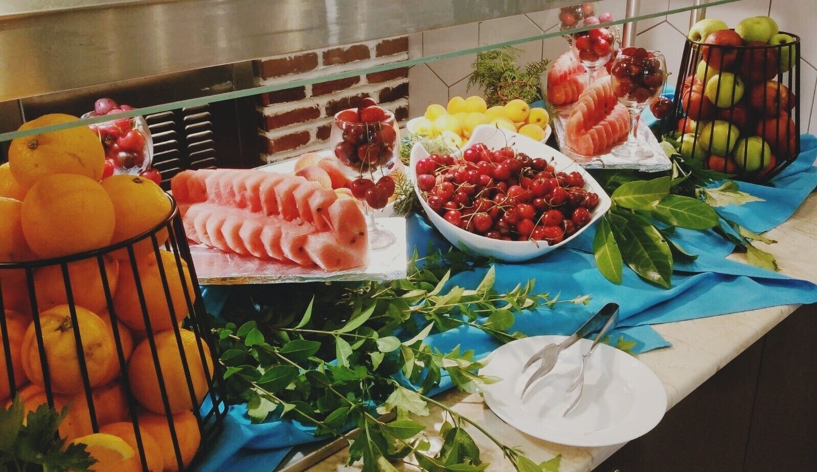 A buffet table with various fruits and vegetables, including oranges, cherries, and sliced watermelon.