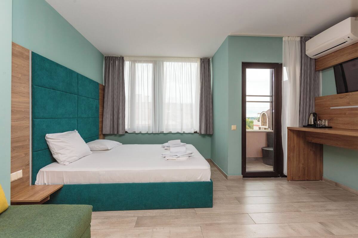 A hotel room with a bed, a desk, a TV, and a window with curtains.