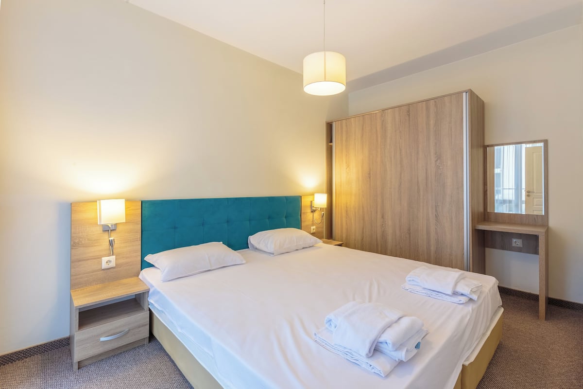 A hotel room with a large bed, two bedside tables, a wardrobe, and a mirror.