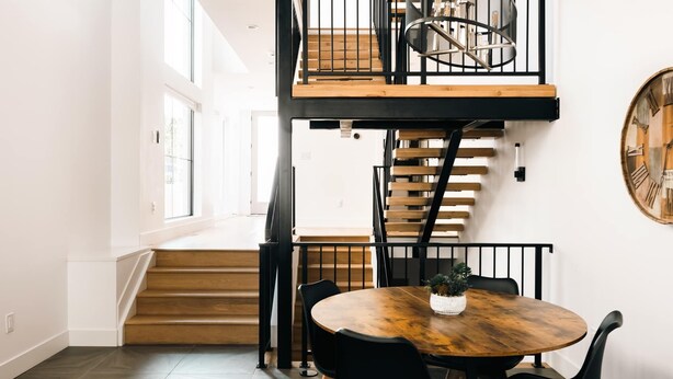 A modern interior with a spiral staircase, a round wooden table, and black chairs.