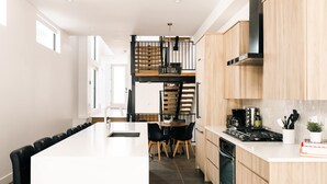 A modern kitchen with a central island, wooden cabinets, a stove, and a dining area with chairs.
