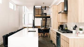 A modern kitchen with a central island, wooden cabinets, a stove, and a dining area with chairs.