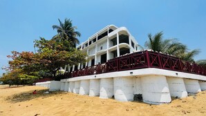 Un hotel frente a la playa con fachada blanca, varios balcones y barandilla roja.