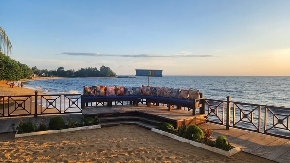 A beachside deck with a wooden bench and railing, overlooking the sea. - la perle de kribi hôtel (Kribi)