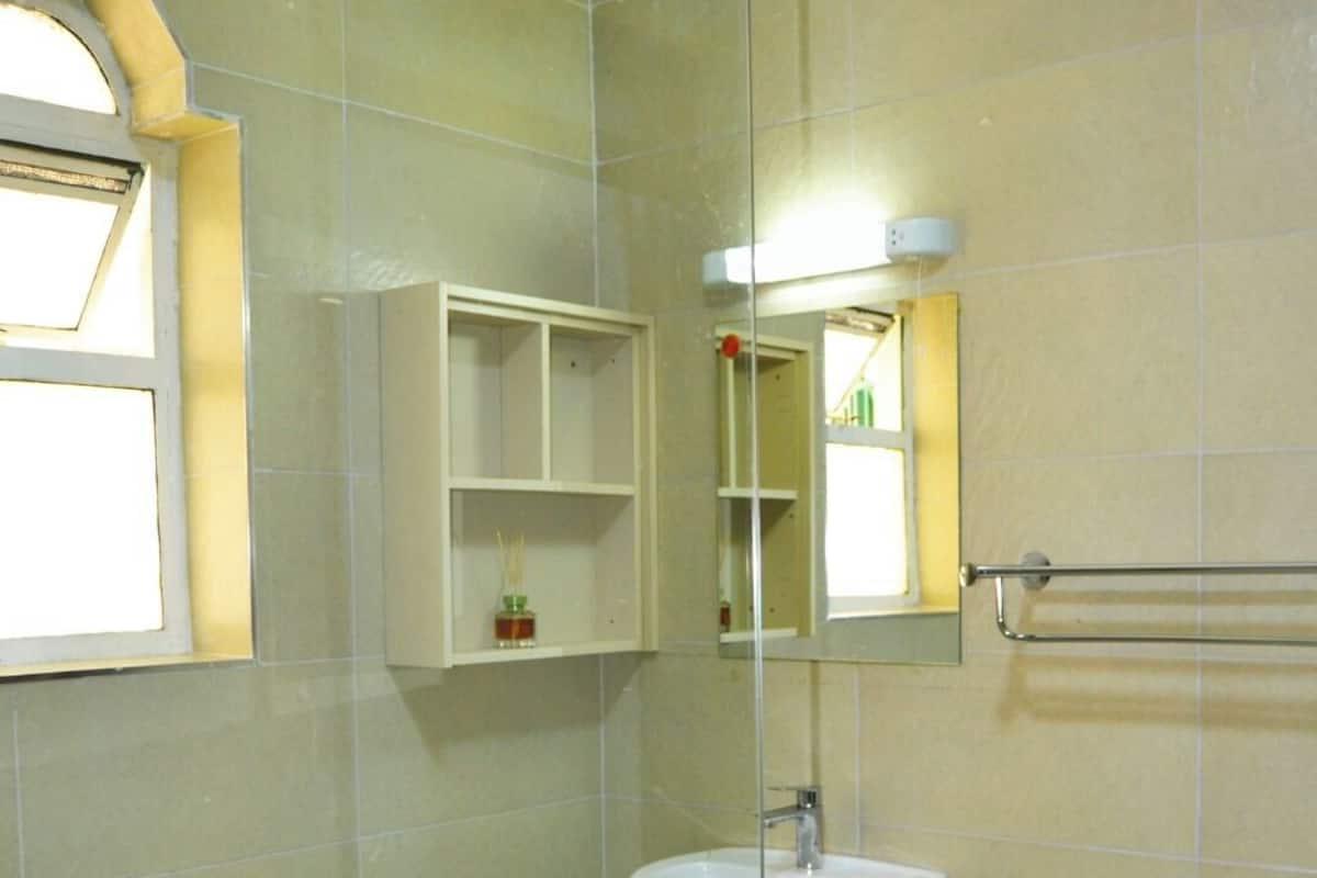 Een badkamer met een douchecabine van glas, een witte wastafel en een spiegel erboven.
