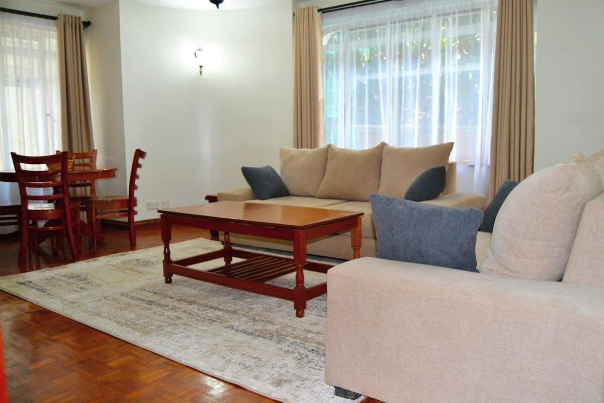Een woonkamer met een bank, een houten salontafel, een eettafel met stoelen en een vloerkleed.