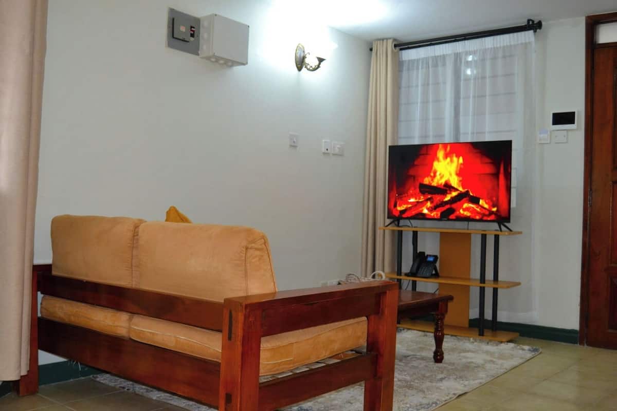 Een woonkamer met een bank, een televisie waarop een haard te zien is, een telefoon en een wandlamp.