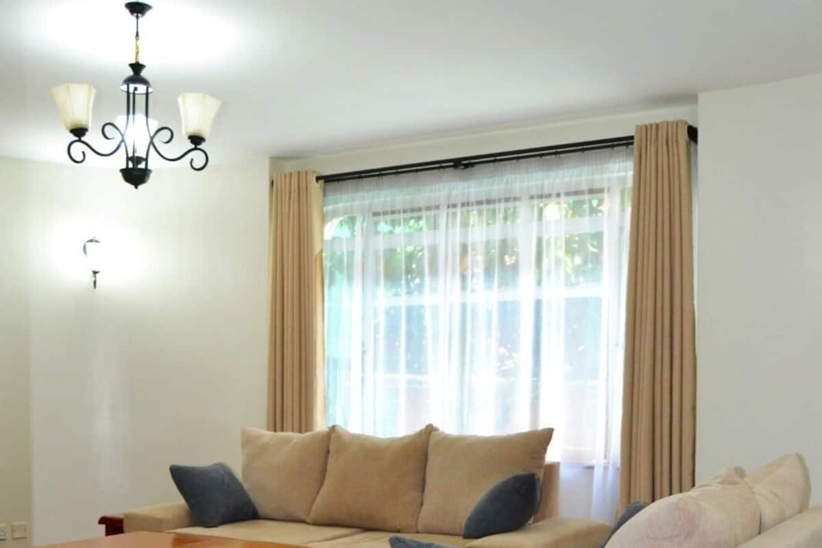 Een woonkamer met een bank, een houten bijzettafeltje, een kroonluchter en een raam met gordijnen.