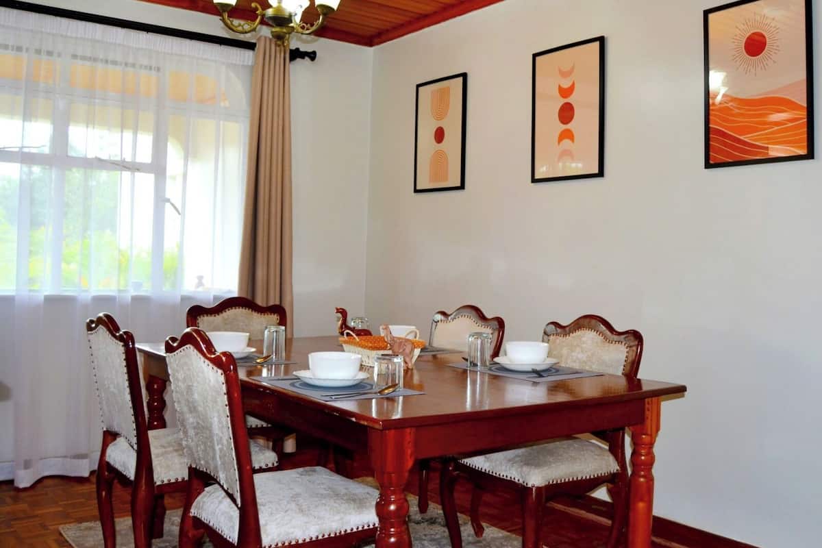 Een eetkamer met een houten tafel, zes stoelen en drie ingelijste kunstwerken aan de muur.