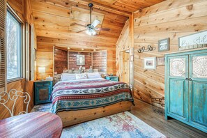 Quarto de cabana de madeira com cama, mesa de cabeceira, cômoda e ventilador de teto.