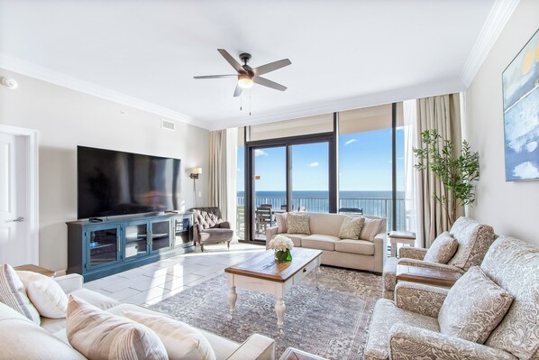 Amplia sala de estar con un televisor de pantalla plana grande, un ventilador de techo y un balcón con vista al mar.