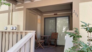 Um deck de madeira com mesa e cadeiras, uma porta de correr de vidro e o número '231' na parede.
