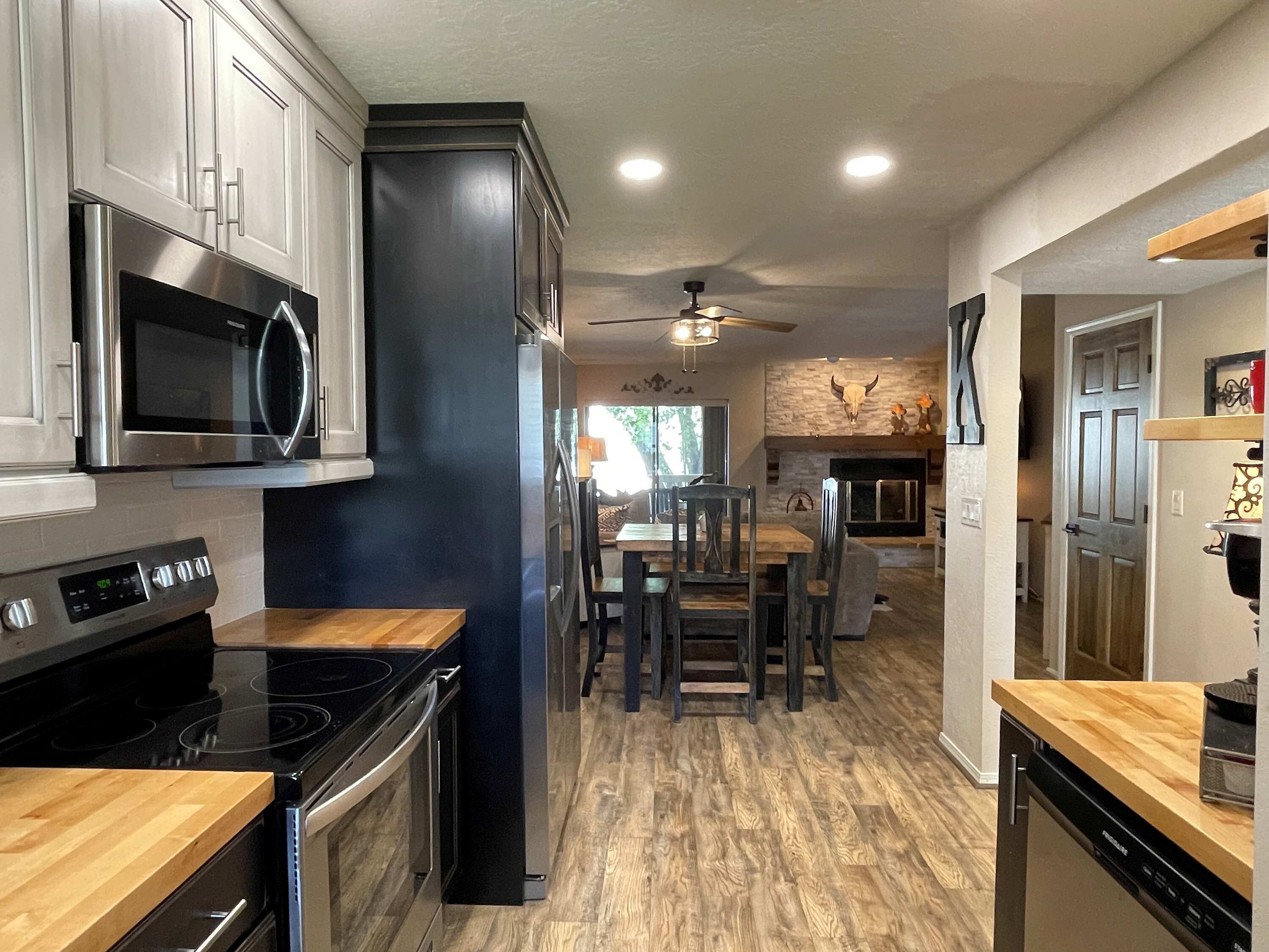 A modern kitchen with stainless steel appliances, a dining area with wooden chairs, and a stone fireplace.