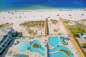 Resort com ampla área de piscina, praia com guarda-sóis e vista para o oceano.