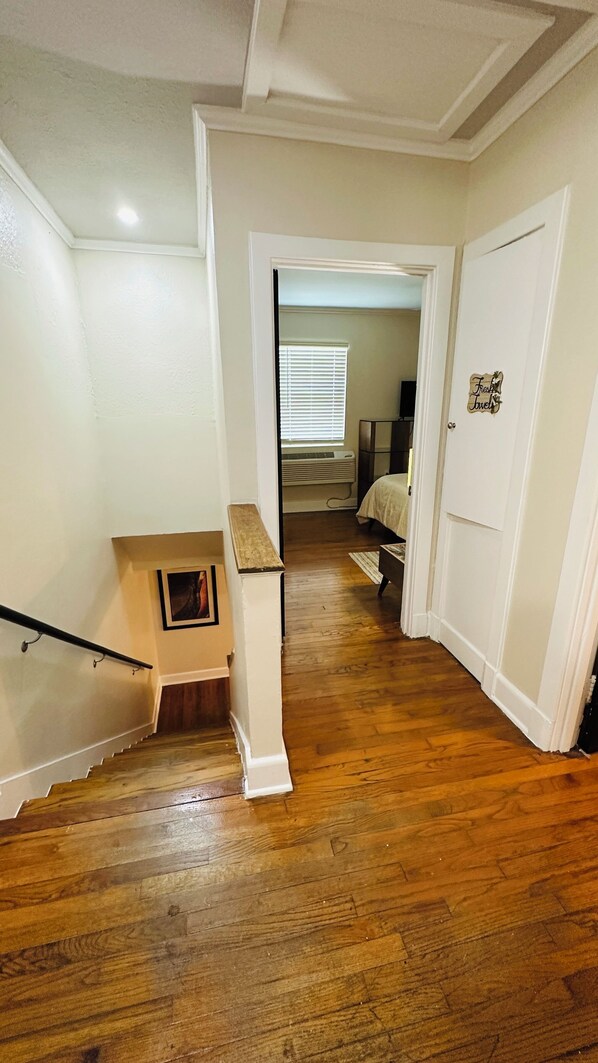 A hallway with wooden flooring, white walls, and a staircase with a wooden handrail.