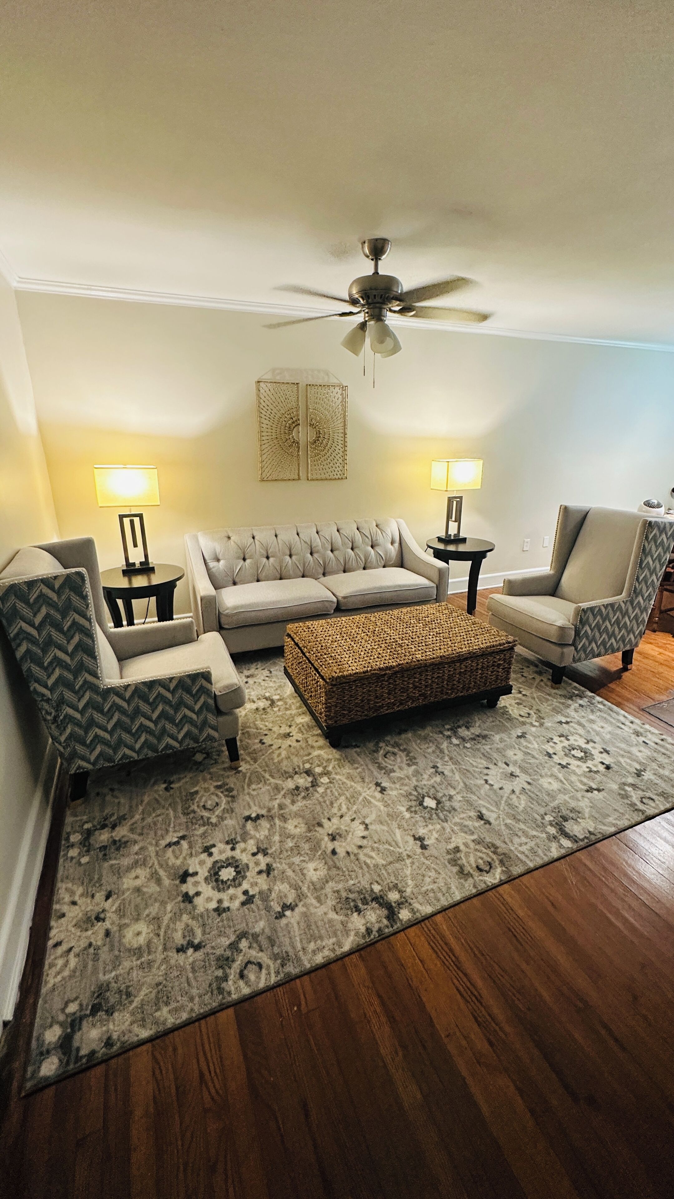A living room with a ceiling fan, a sofa, two armchairs, a coffee table, and two lamps.