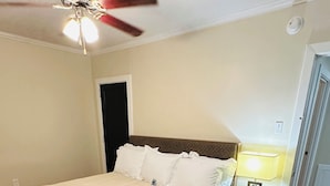 A bedroom with a bed, a nightstand with a lamp, a ceiling fan, and a door. - Charming 2-Bedroom Condo in Baton Rouge close to LSU and Downtown (Baton Rouge)