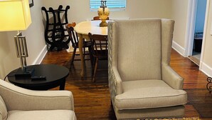 A living room with a sofa, armchair, and ottoman, a dining table with chairs, a lamp, and a chandelier. - Charming 2-Bedroom Condo in Baton Rouge close to LSU and Downtown (Baton Rouge)