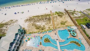 Vista aérea de un complejo turístico en la playa con una gran piscina, sombrillas de playa y un paseo marítimo de madera.
