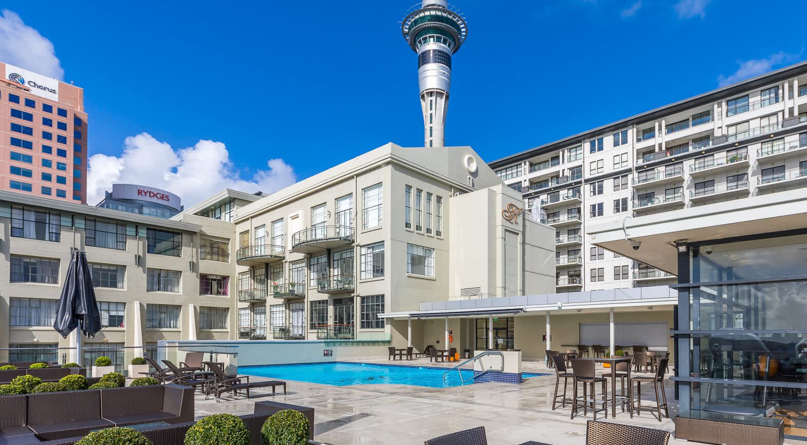 A hotel with a swimming pool, outdoor seating, and a view of a tower.