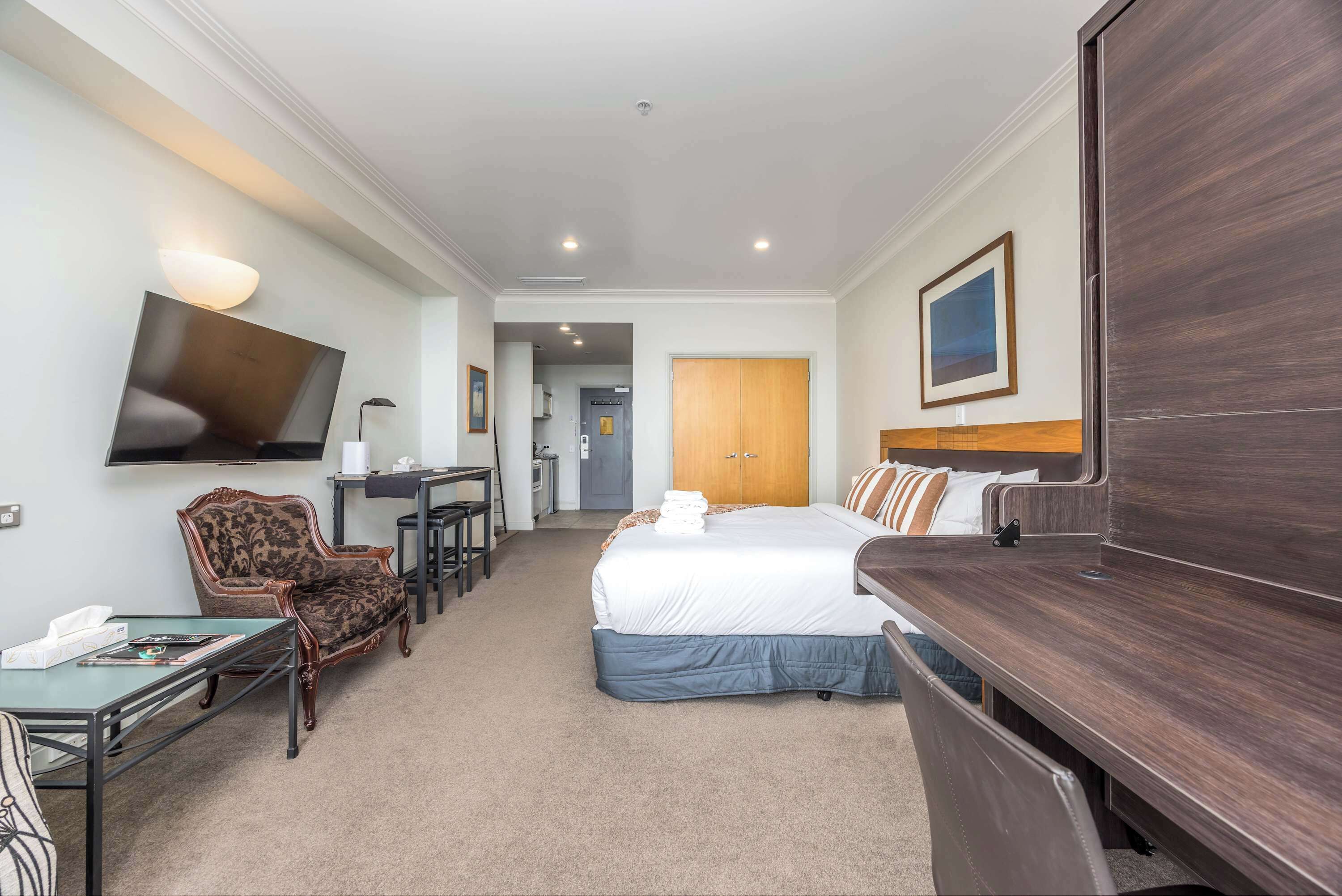 Ein Hotelzimmer mit Bett, Schreibtisch, Stuhl, Fernseher und Kleiderschrank.