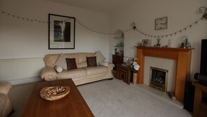 Een woonkamer met een beige bank, een houten salontafel, een open haard en lichtslingers.