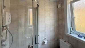 Een moderne badkamer met een glazen douchecabine, een toilet en een raam met decoratief glas.