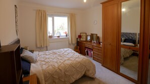 Een slaapkamer met een bed, een kaptafel, een spiegel en een raam met gordijnen.