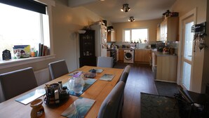 Een moderne keuken met een eethoek, houten kastjes, een inbouwoven en een groot raam dat voor natuurlijk licht zorgt.