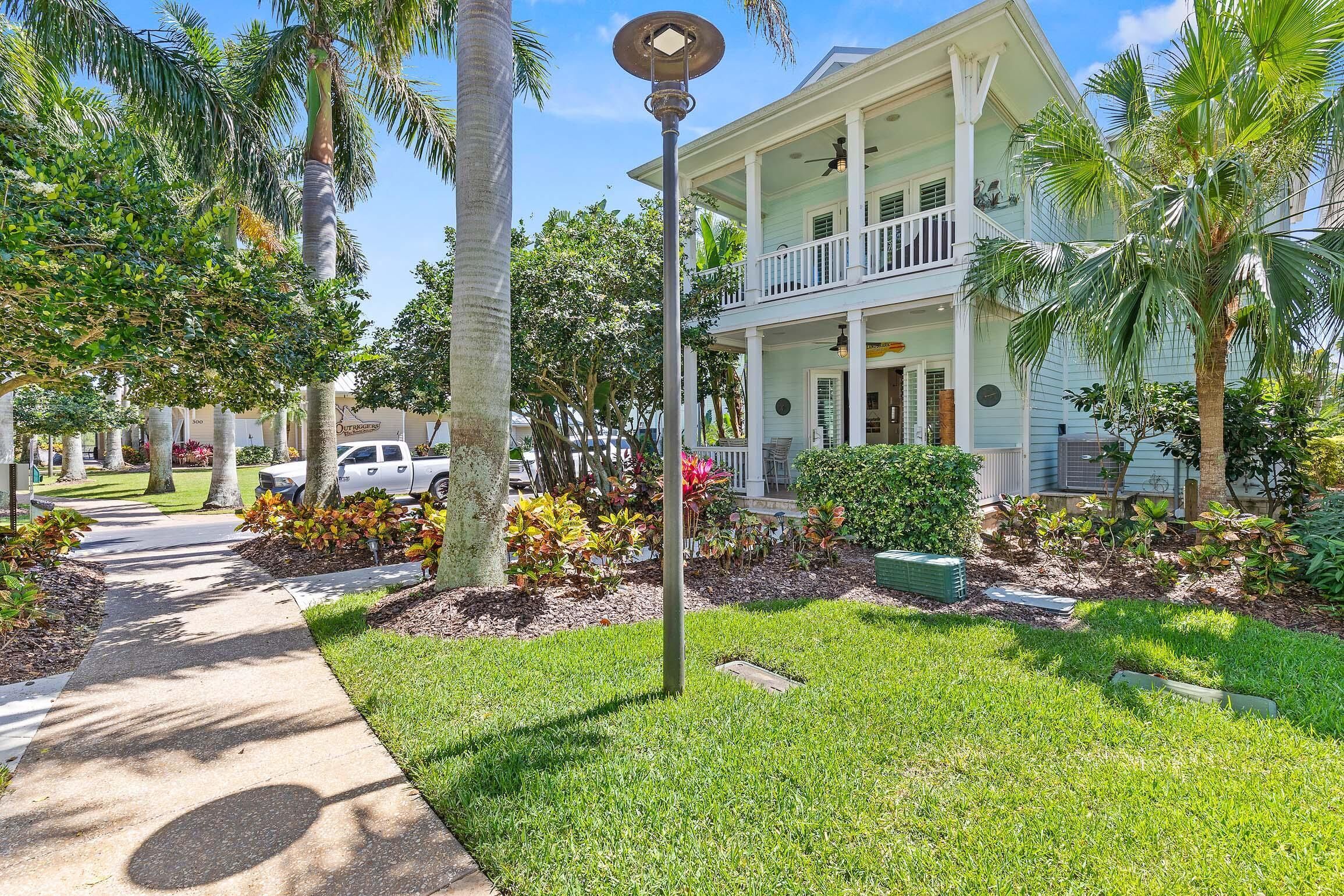A two-story building with a balcony, surrounded by palm trees and a well-maintained lawn.