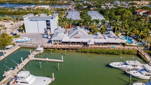 Un puerto deportivo con barcos amarrados, un edificio grande con el letrero "New Smyrna Marina" y una zona de piscina con sombrillas.