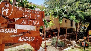 Un cartel de madera rústico con indicaciones hacia 'Turismo Rural Sol de Altura', 'Cabañas' y 'Achalay'.
