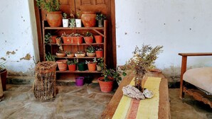 Un interior rústico con una silla de madera, una mesa con un posavasos tejido y una estantería de madera con varias macetas.
