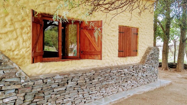 Un edificio rústico con base de piedra, contraventanas de madera y pared exterior amarilla.