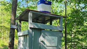 A portable restroom with a sign instructing to make showers short, surrounded by trees. - Small family & pet friendly campground. Easy access to many public beaches. (Hartington)